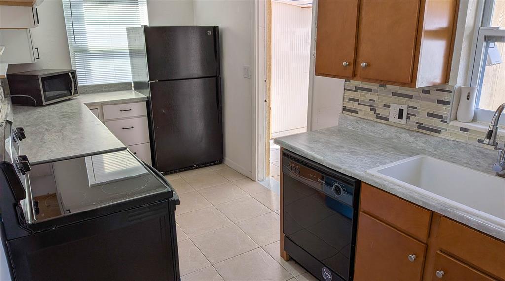 A kitchen features wood cabinets, a black refrigerator, a black dishwasher, and light-colored countertops — 11301 110TH TERRACE, LARGO, FL