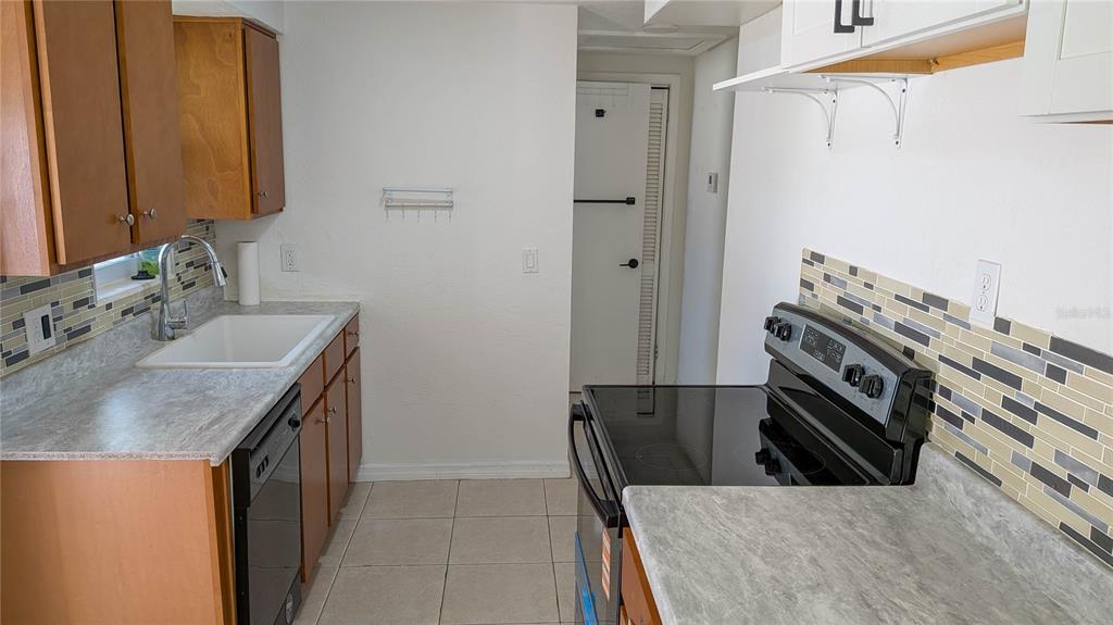 A kitchen features wood cabinets, a white sink, a black stove, and a tiled backsplash — 11301 110TH TERRACE, LARGO, FL