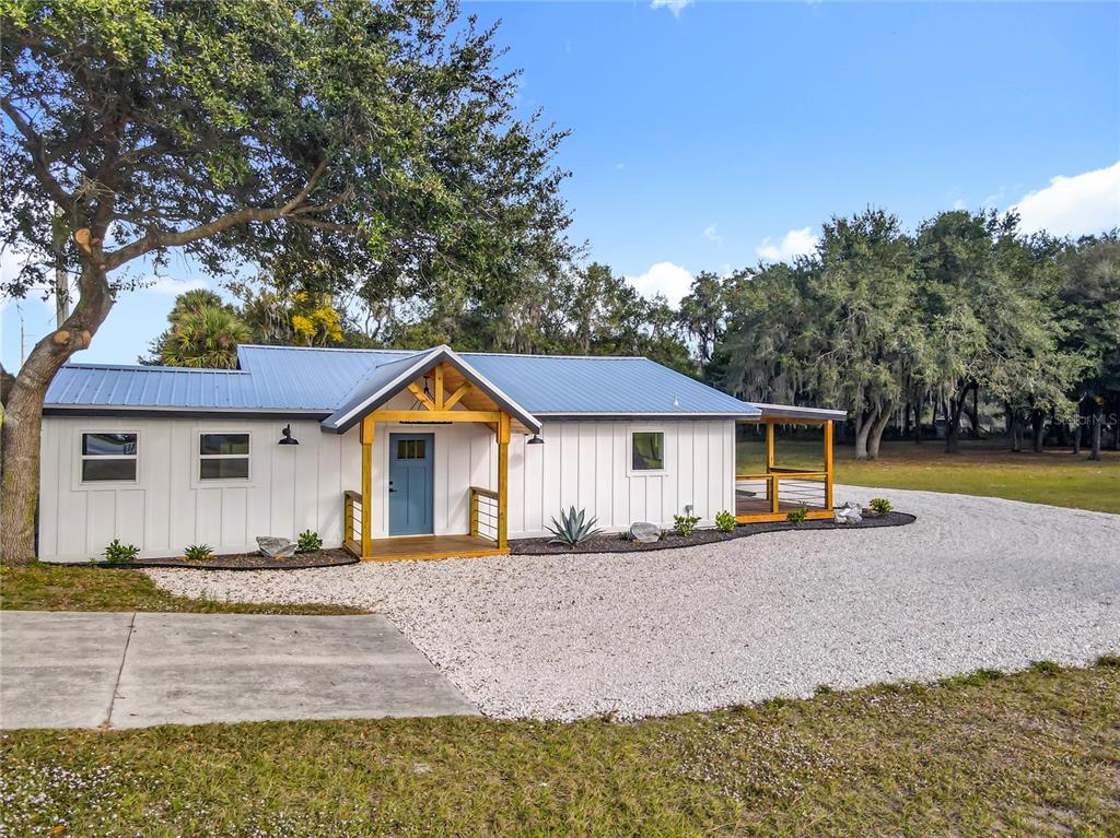 A white farmhouse-style home with a blue metal roof and a wooden front porch — 379 N SR 415, OSTEEN, FL