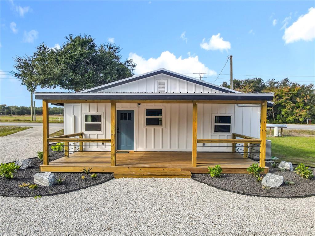 A white house with a covered wooden porch and gravel landscaping under a blue sky — 379 N SR 415, OSTEEN, FL