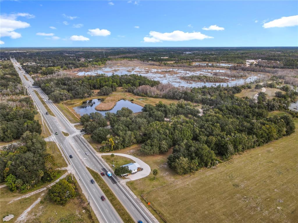 An aerial view shows a house situated next to a highway, wetlands, and open fields — 379 N SR 415, OSTEEN, FL