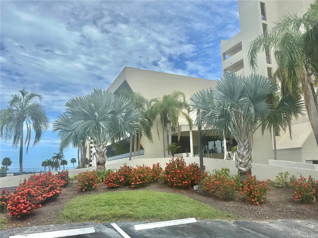 A multi-story building exterior features palm trees and red flowering shrubs in the foreground — 5915 SEA RANCH DRIVE UNIT 711, HUDSON, FL