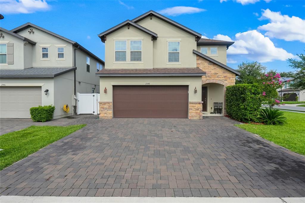 A two-story suburban townhouse with a tan stucco exterior, stone accents, and a paved driveway — 2948 CREST DRIVE, KISSIMMEE, FL