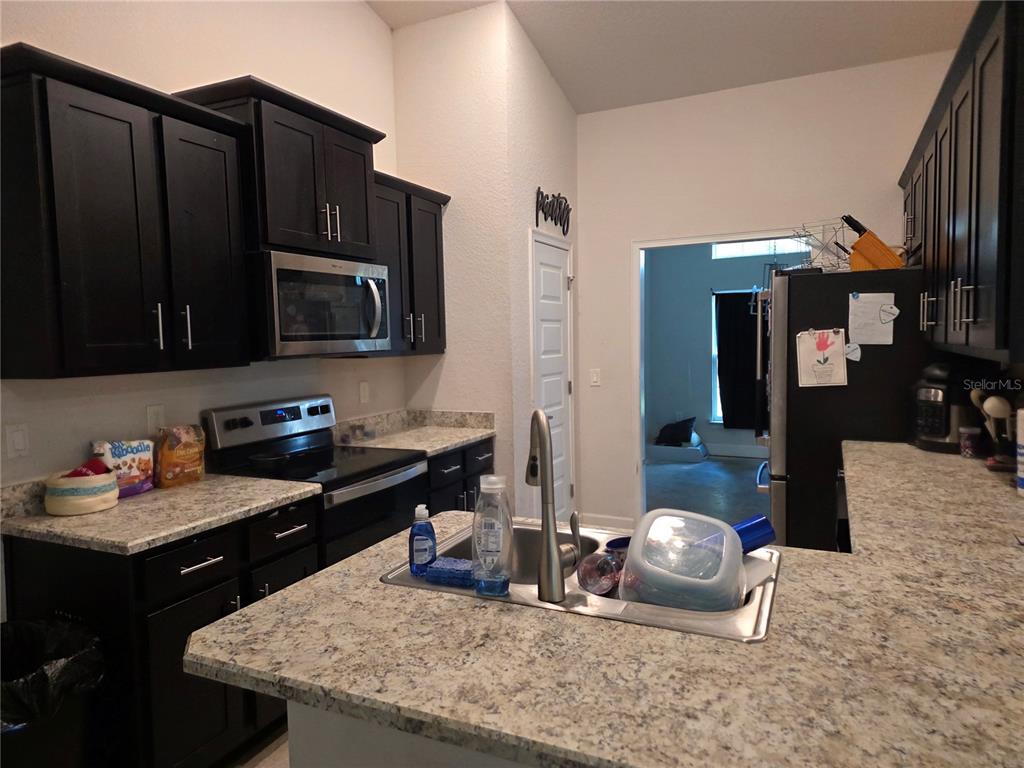 A kitchen features dark wood cabinets, granite countertops, stainless steel appliances, and a central sink — 9 CEDAR RUN, OCALA, FL