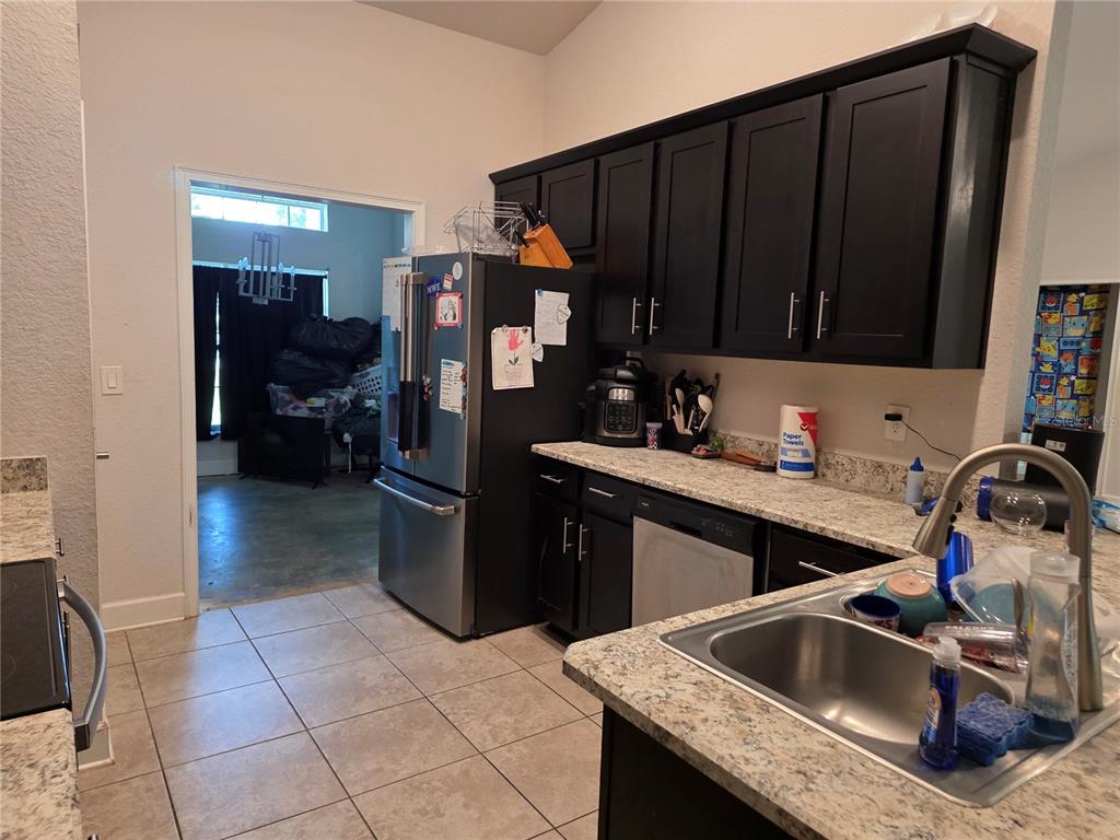 A kitchen features dark cabinets, granite countertops, a stainless steel refrigerator, and a double sink — 9 CEDAR RUN, OCALA, FL