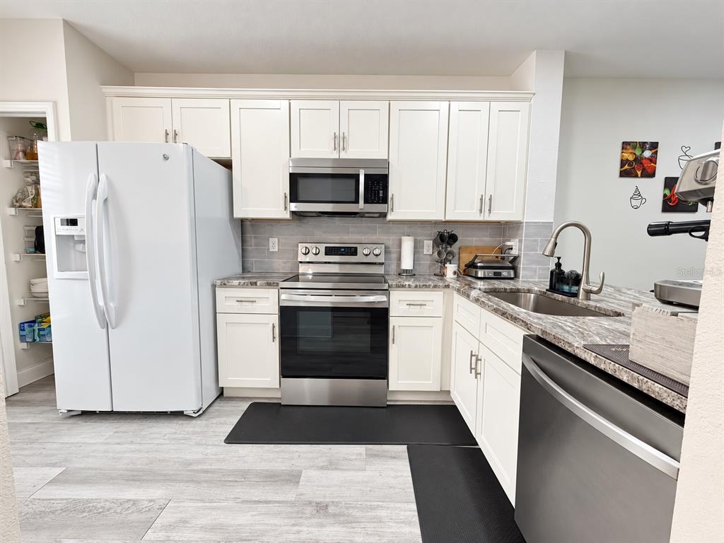 A kitchen features white cabinets, stainless steel appliances, a grey tiled backsplash, and wood-look flooring — 2334 LAKE WOODBERRY CIRCLE, BRANDON, FL