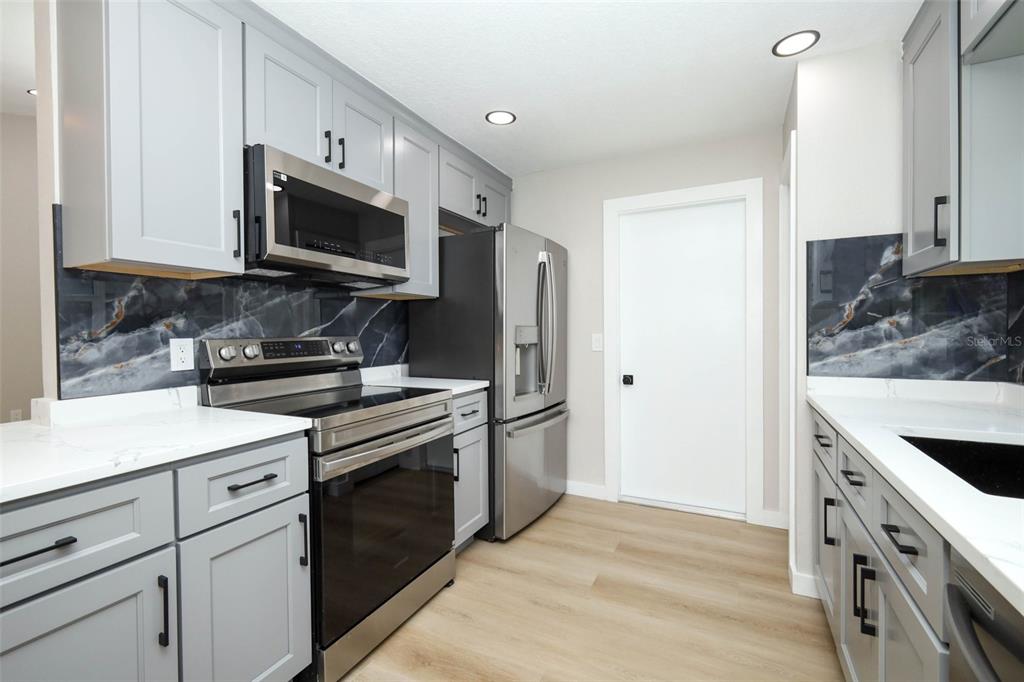 A kitchen with gray cabinets, stainless steel appliances, and a dark marble-patterned backsplash — 761 ROBINHOOD DRIVE, MAITLAND, FL
