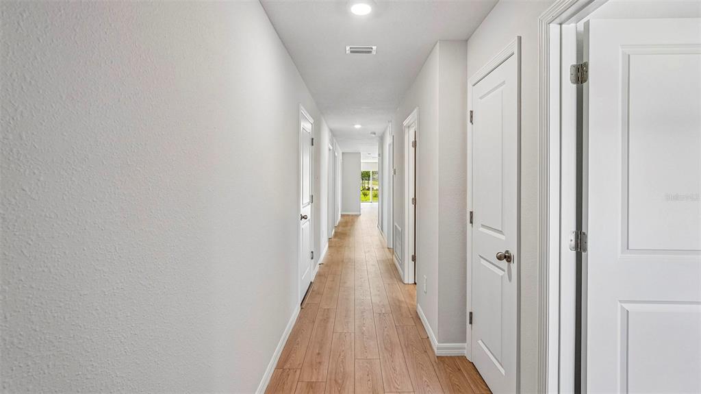 A long hallway with light wood-look flooring and white doors leads toward a bright doorway — 13129 OLD CANOE WAY, PARRISH, FL