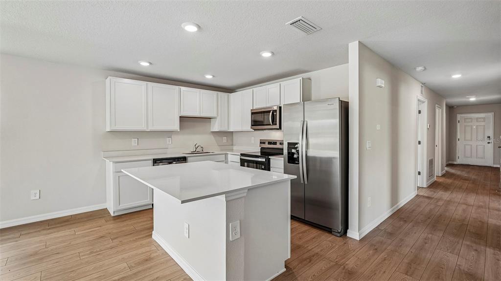 A modern kitchen features white cabinets, stainless steel appliances, a center island, and wood flooring — 13129 OLD CANOE WAY, PARRISH, FL