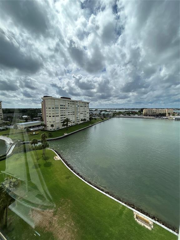 An elevated view of a waterfront apartment building, a grassy lawn, and a large bay — 4775 COVE CIRCLE UNIT 1202, MADEIRA BEACH, FL