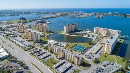 An aerial view shows several multi-story apartment buildings surrounding a small lake near the ocean — 4775 COVE CIRCLE UNIT 1202, MADEIRA BEACH, FL