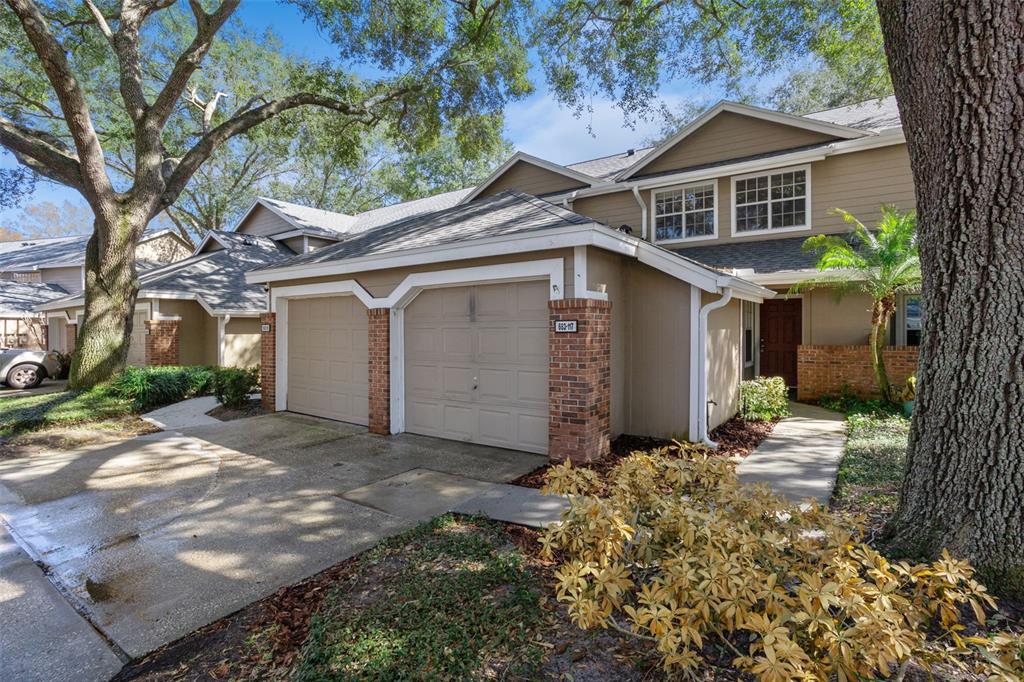 A two-story townhouse with a two-car garage, brick accents, and mature trees in front — 683 POST OAK CIRCLE UNIT 117, ALTAMONTE SPRINGS, FL