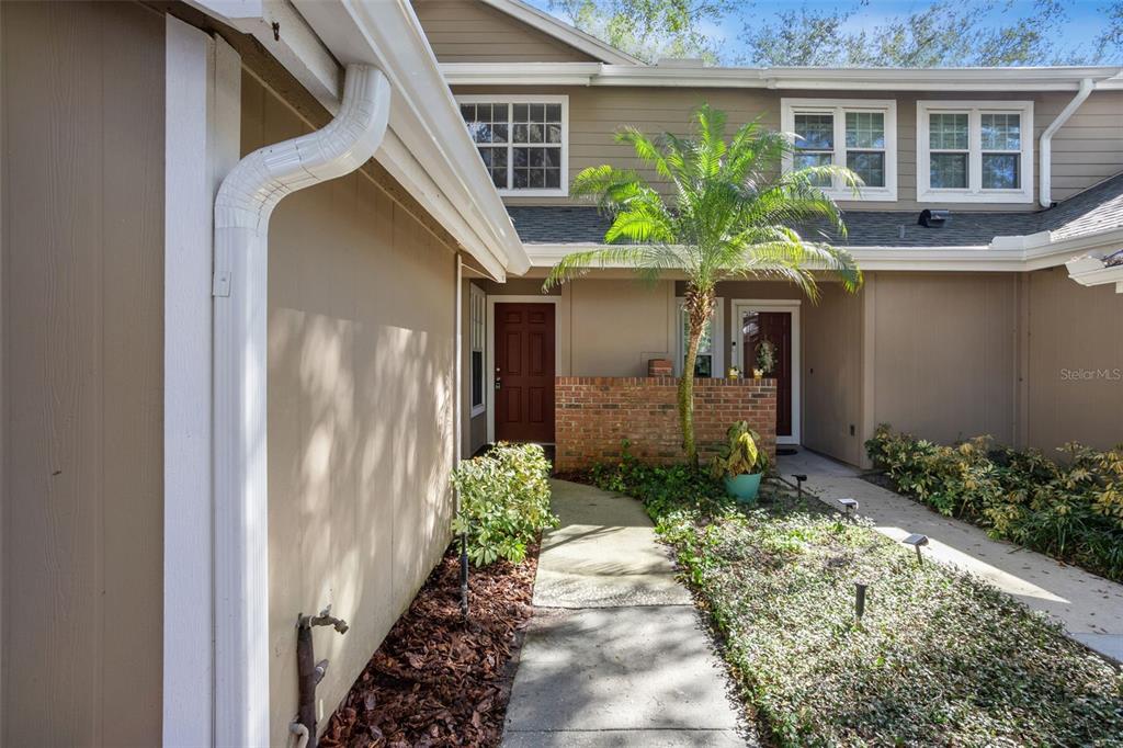 A tan townhouse exterior features a brick wall, a palm tree, and a concrete walkway — 683 POST OAK CIRCLE UNIT 117, ALTAMONTE SPRINGS, FL
