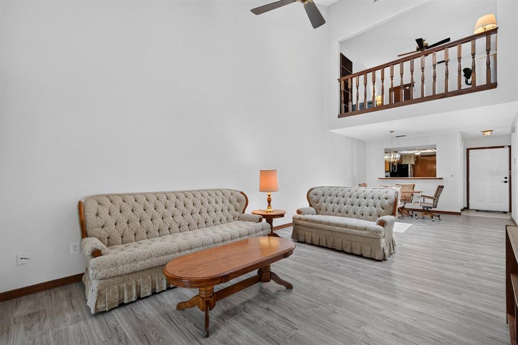 A living room features light wood-look flooring, a wooden bookshelf, and sliding glass doors — 357 CASTLEWOOD LANE, NEW SMYRNA BEACH, FL
