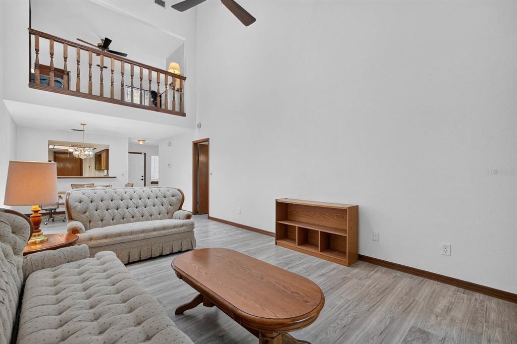 A living room with high ceilings, tufted sofas, a wooden coffee table, and wood-look flooring — 357 CASTLEWOOD LANE, NEW SMYRNA BEACH, FL