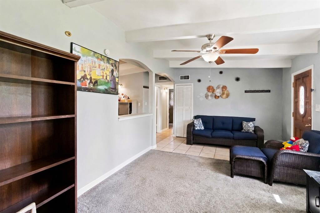 A living room with a blue sofa, wicker armchair, ceiling fan, and a large bookshelf — 1311 WINDSOR WAY, TAMPA, FL