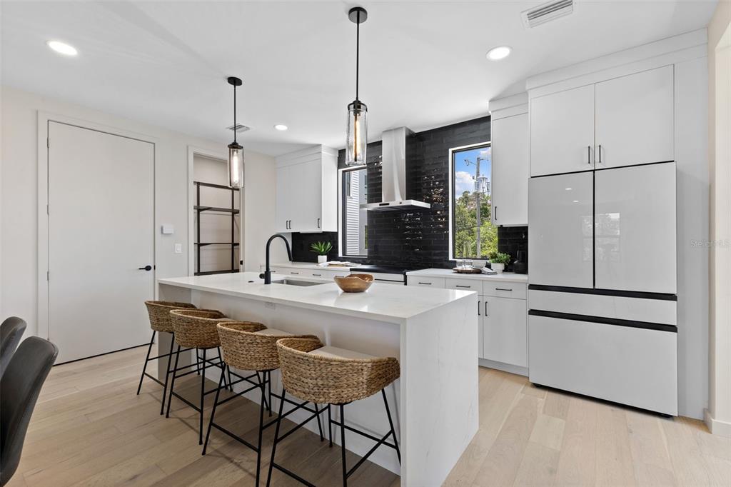 A modern kitchen features white cabinetry, a marble-topped island with woven stools, and black tile — 2211 16TH STREET N, ST PETERSBURG, FL