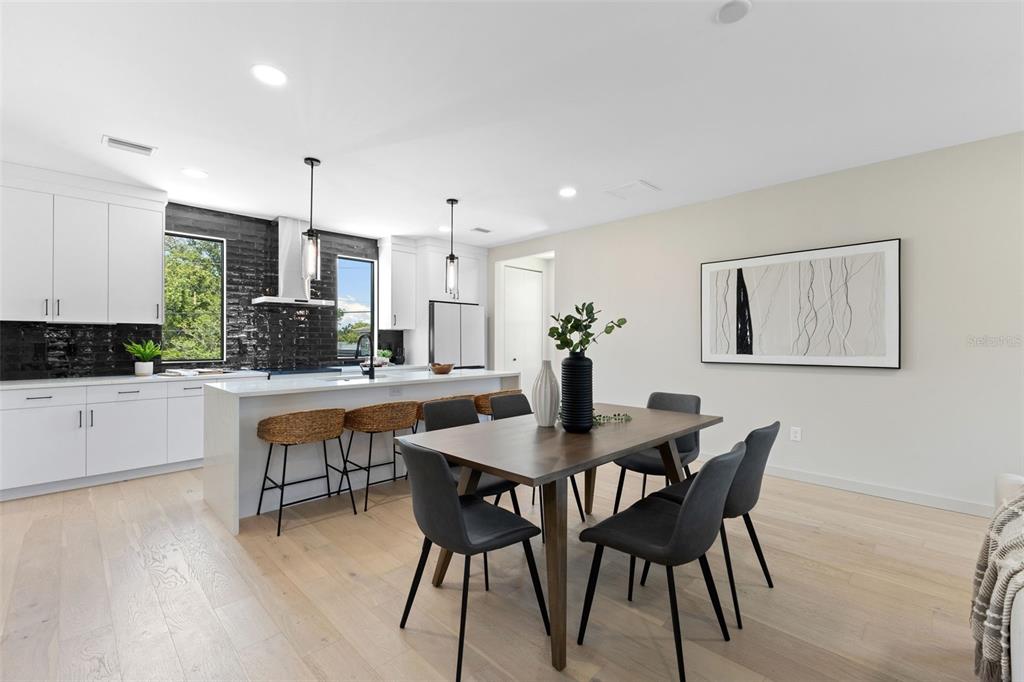 A modern kitchen and dining area features white cabinetry, a black tile backsplash, and wood floors — 2211 16TH STREET N, ST PETERSBURG, FL