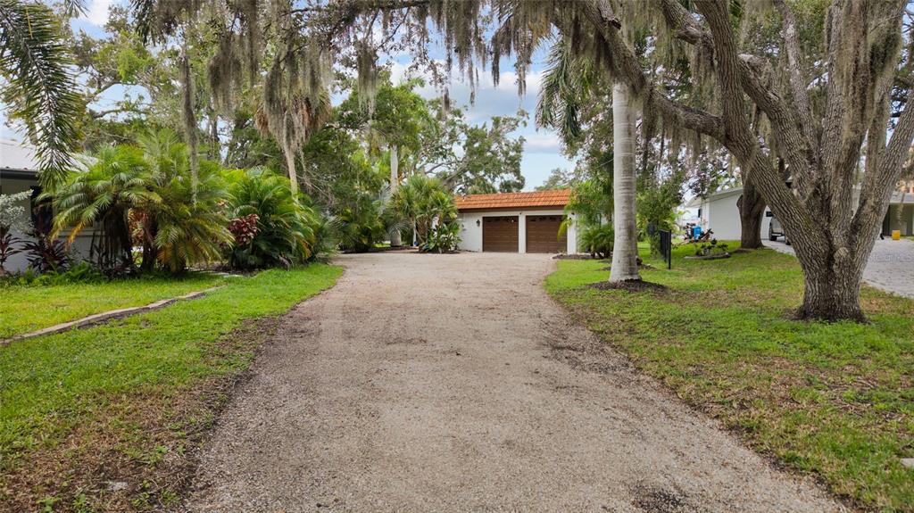 A gravel driveway leads to a detached two-car garage surrounded by trees and landscaping — 5381 PALOS VERDES DRIVE, SARASOTA, FL