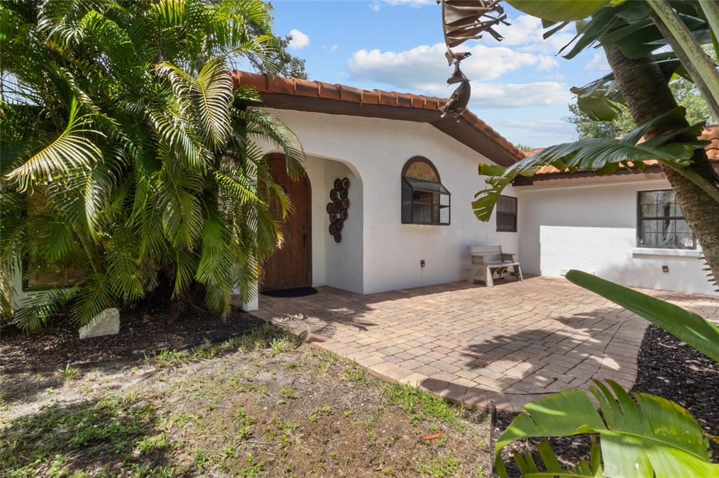 A white house exterior features a tiled roof, arched wooden door, and a brick patio — 5381 PALOS VERDES DRIVE, SARASOTA, FL