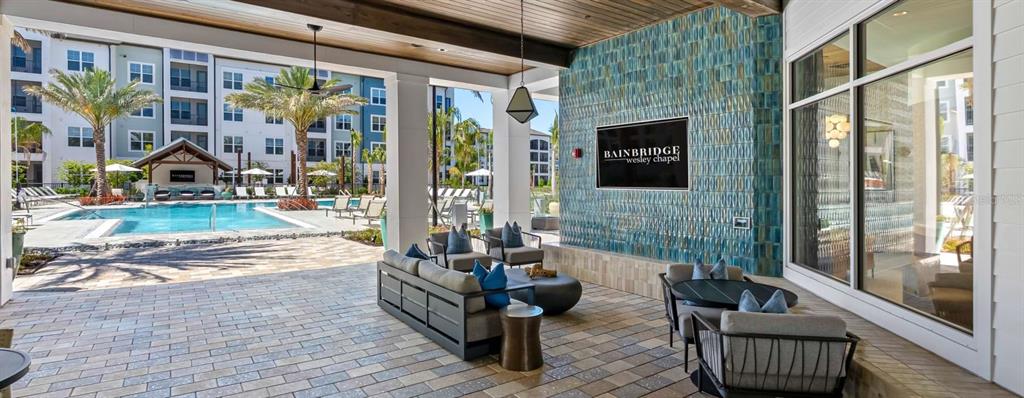 An outdoor lounge area features a blue tiled wall, patio furniture, and a swimming pool — 32475 SUGARPLUM LOOP UNIT 4201, WESLEY CHAPEL, FL