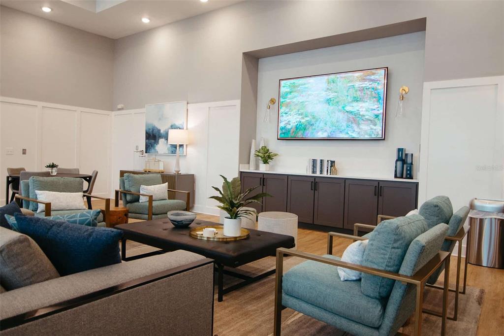 A modern living room features teal armchairs, a dark coffee table, and a wall-mounted television — 32475 SUGARPLUM LOOP UNIT 4201, WESLEY CHAPEL, FL