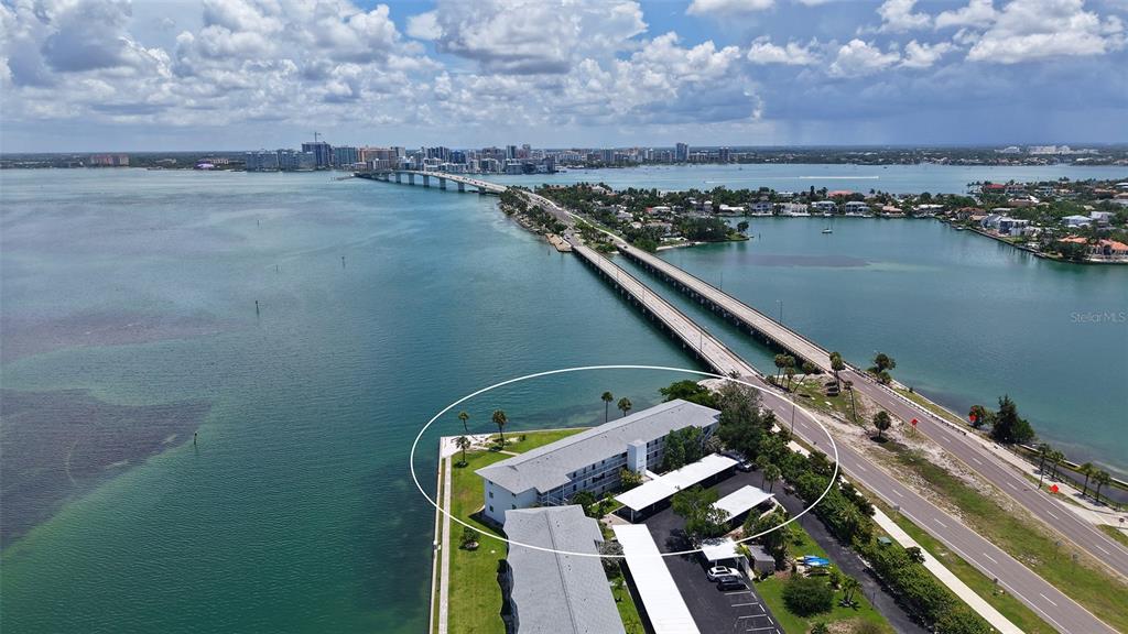 An aerial view shows a multi-story apartment building situated on a waterfront peninsula near a bridge — 777 JOHN RINGLING BOULEVARD UNIT 24, SARASOTA, FL