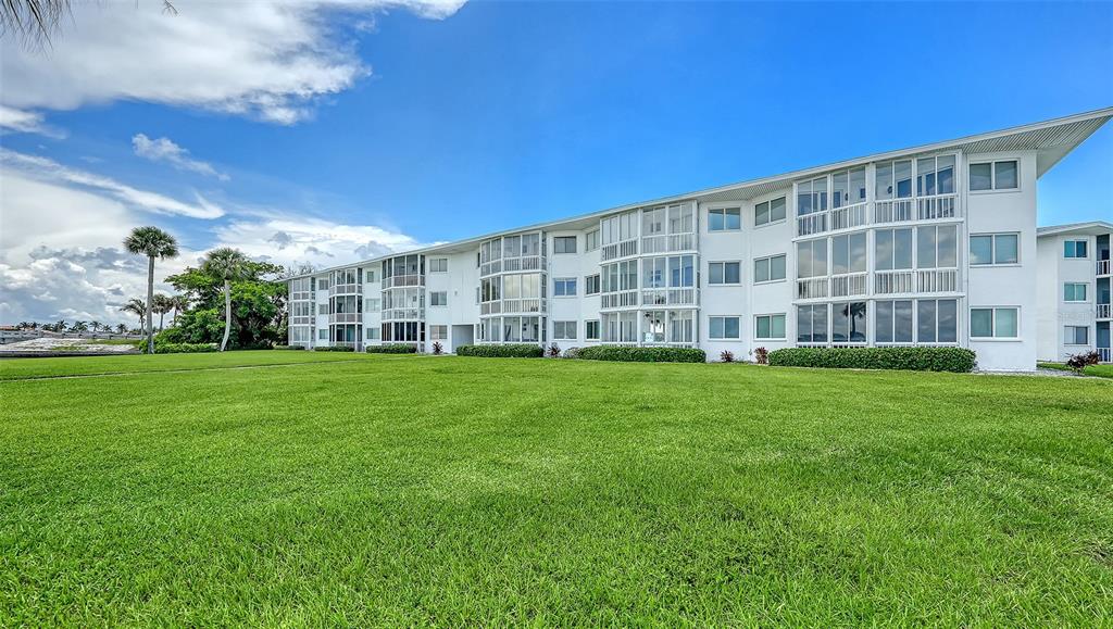A multi-story white apartment building sits behind a large, manicured green lawn — 777 JOHN RINGLING BOULEVARD UNIT 24, SARASOTA, FL