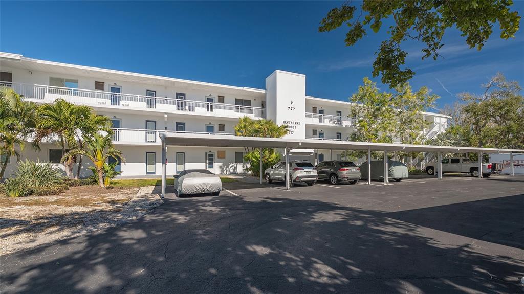 A three-story white apartment building features a covered parking area with several parked cars — 777 JOHN RINGLING BOULEVARD UNIT 24, SARASOTA, FL