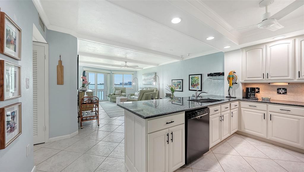 A kitchen with white cabinets and granite countertops opens into a living area with water views — 777 JOHN RINGLING BOULEVARD UNIT 24, SARASOTA, FL