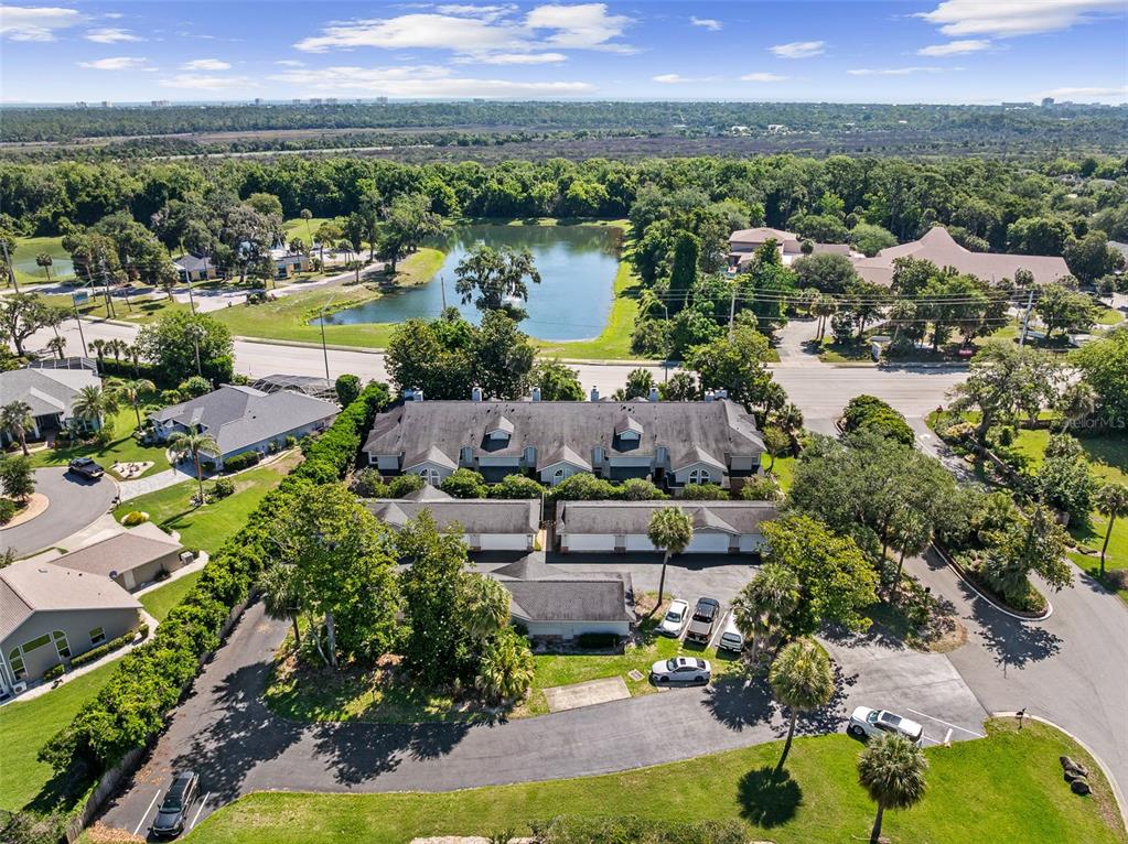 An aerial view shows a multi-unit residential building with garages, parking, and a nearby pond — 596 N NOVA ROAD UNIT 308, ORMOND BEACH, FL