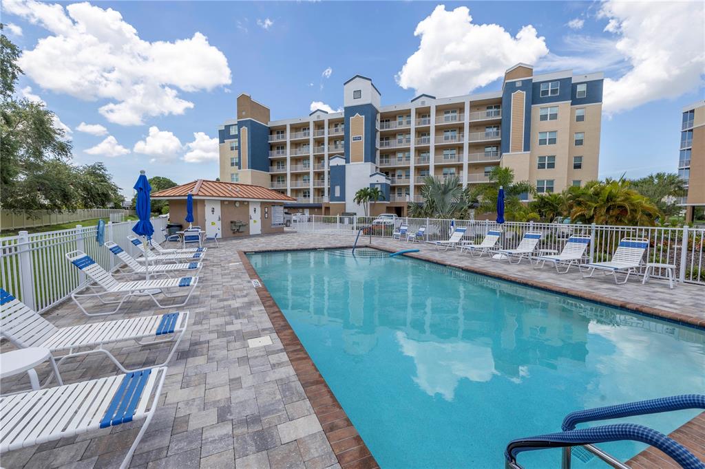 A swimming pool with lounge chairs sits in front of a multi-story apartment building — 960 STARKEY ROAD UNIT 2202, LARGO, FL