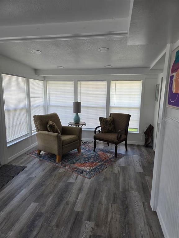 A sunroom features wood-look flooring, large windows with blinds, and two armchairs on a rug — 5247 ALPACA DRIVE, WEEKI WACHEE, FL
