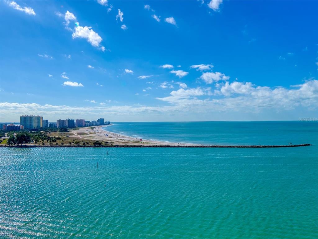 An aerial view of a sandy beach, a long jetty, and distant high-rise buildings — 450 GULFVIEW BOULEVARD S UNIT 1708, CLEARWATER, FL