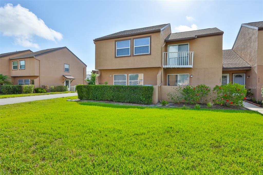 A two-story tan townhouse with a balcony and a green lawn in front — 1865 CLEARBROOKE DRIVE, CLEARWATER, FL