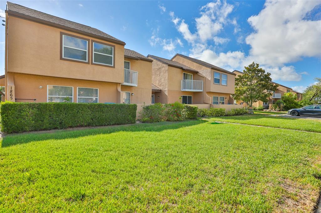 A row of two-story tan stucco townhomes with balconies and a manicured lawn — 1865 CLEARBROOKE DRIVE, CLEARWATER, FL