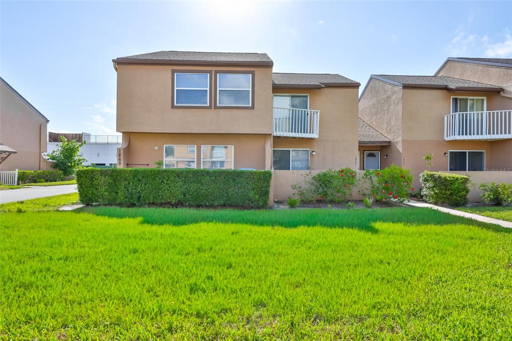 A two-story tan townhouse with a green hedge and a grassy front lawn — 1865 CLEARBROOKE DRIVE, CLEARWATER, FL