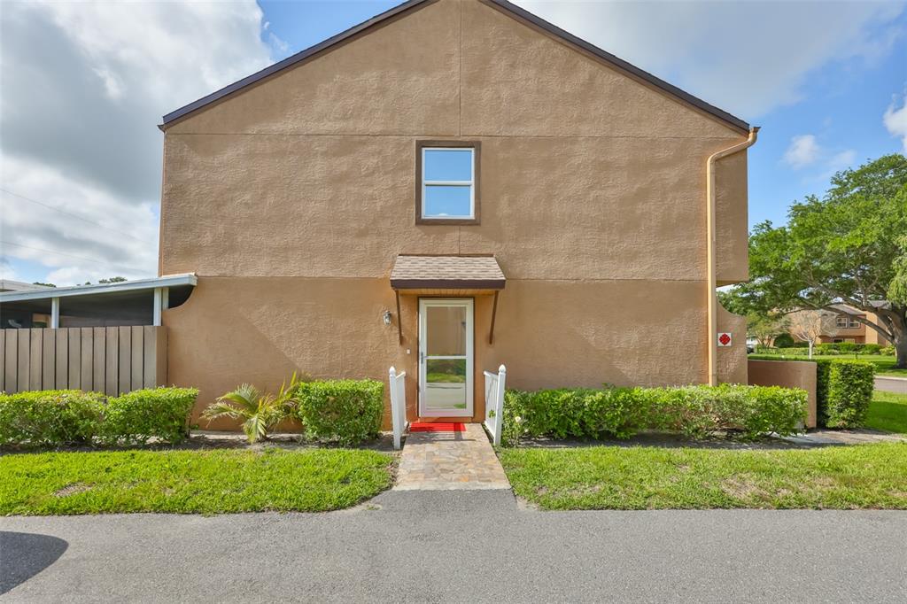 A two-story tan stucco building with a single door, a window, and a stone walkway — 1865 CLEARBROOKE DRIVE, CLEARWATER, FL