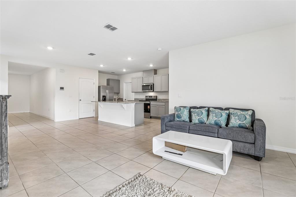 An open-concept living room features tile flooring, a gray sofa, and a kitchen with island — 2945 ELIO HAMMOCK DR, HARMONY, FL