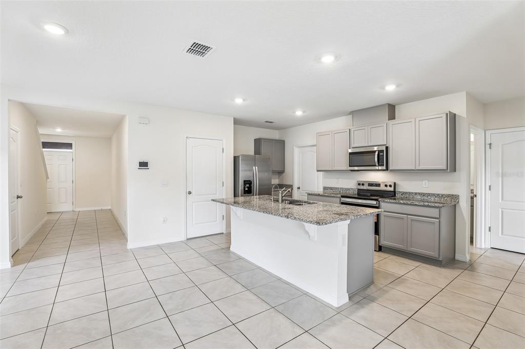 A kitchen features gray cabinets, granite countertops, a center island, and light-colored tile flooring — 2945 ELIO HAMMOCK DR, HARMONY, FL
