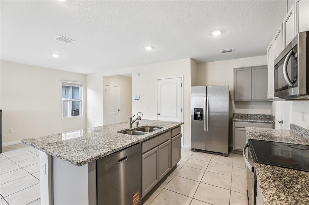 A kitchen features gray cabinets, granite countertops, stainless steel appliances, and a central island — 2945 ELIO HAMMOCK DR, HARMONY, FL