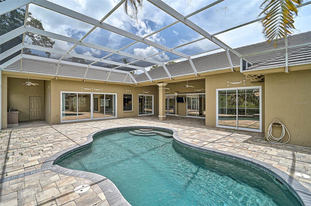 A screened-in patio features a kidney-shaped swimming pool surrounded by light-colored stone pavers — 852 MACEWEN DRIVE, OSPREY, FL
