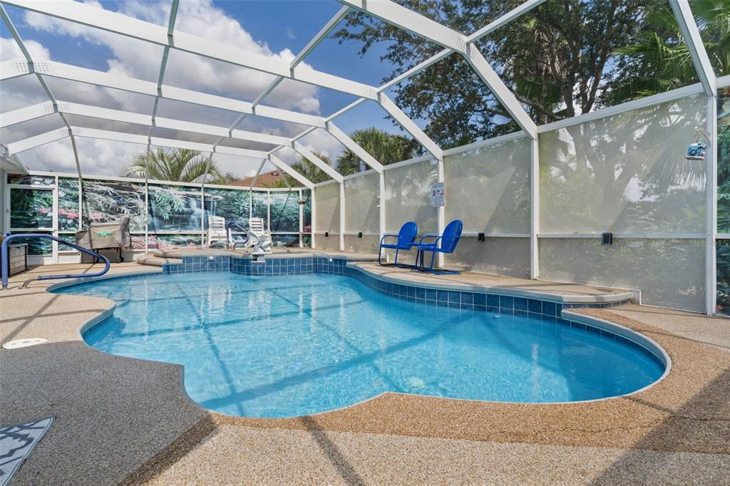A screened-in swimming pool with blue tile trim and a surrounding textured concrete deck — 1555 COPE PLACE, THE VILLAGES, FL