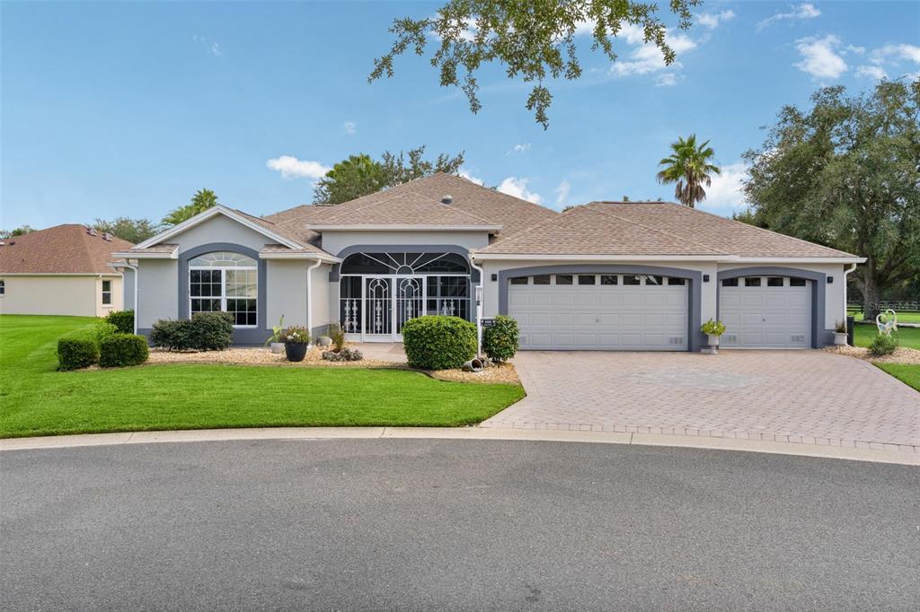 A single-story suburban house with a three-car garage, a screened entryway, and a paved driveway — 1555 COPE PLACE, THE VILLAGES, FL