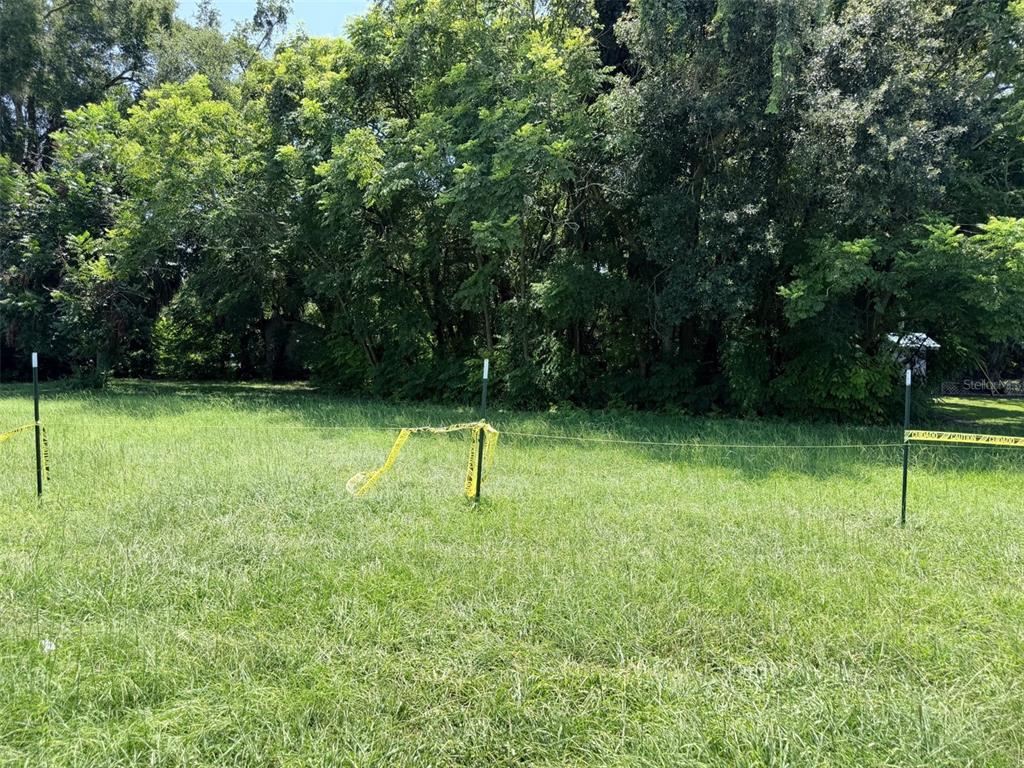 A grassy, undeveloped lot is marked by metal stakes and yellow caution tape — 1005 NW 19TH AVENUE, CHIEFLAND, FL