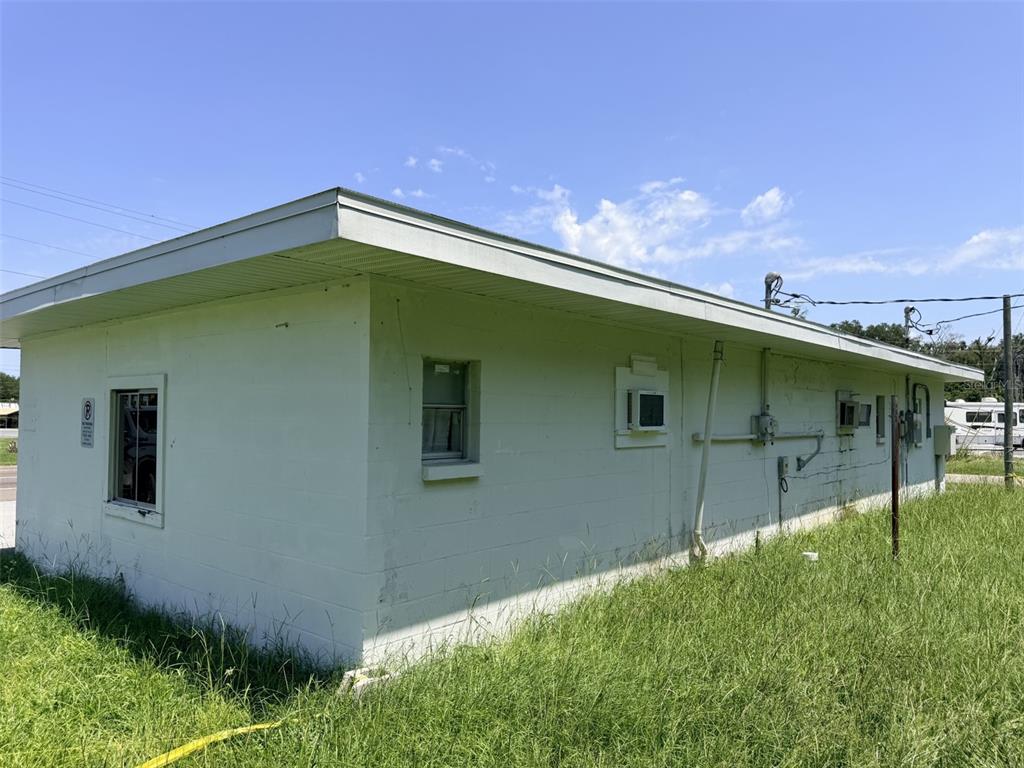 The exterior of a white concrete block building with a flat roof and overgrown grass — 1005 NW 19TH AVENUE, CHIEFLAND, FL