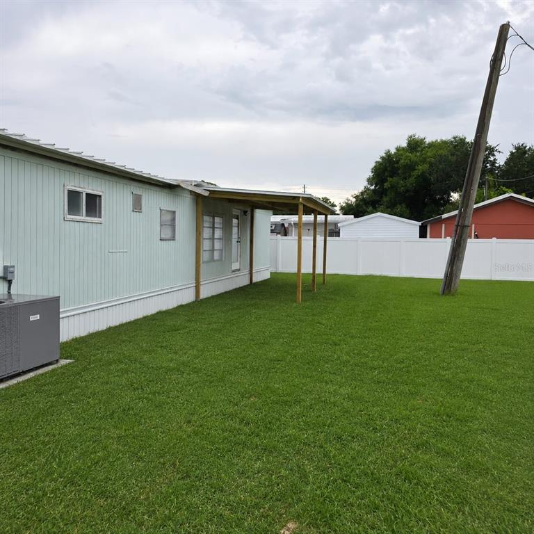 The exterior of a light green mobile home features a wooden carport and a large lawn — 2010 OAK STREET, ST CLOUD, FL