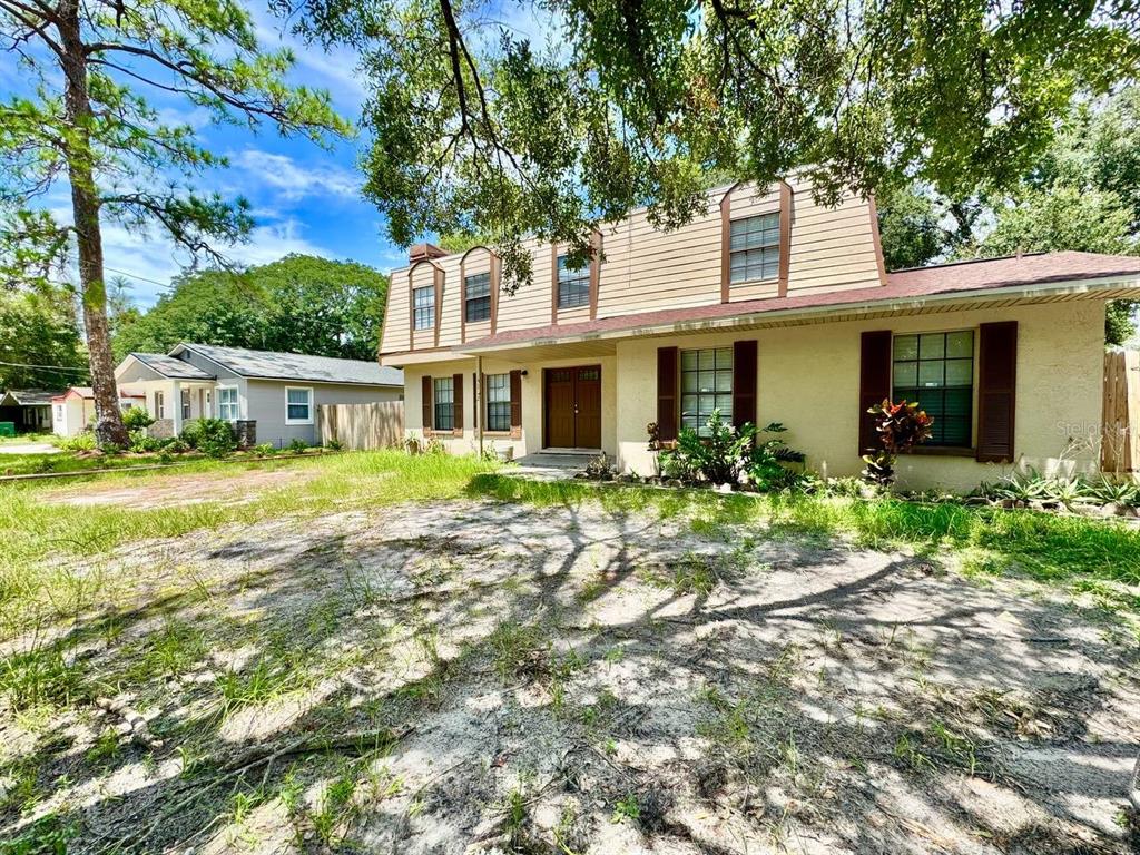 A two-story house with tan siding and brown shutters sits behind a sandy, grassy yard — 5132 CHILKOOT STREET, TAMPA, FL