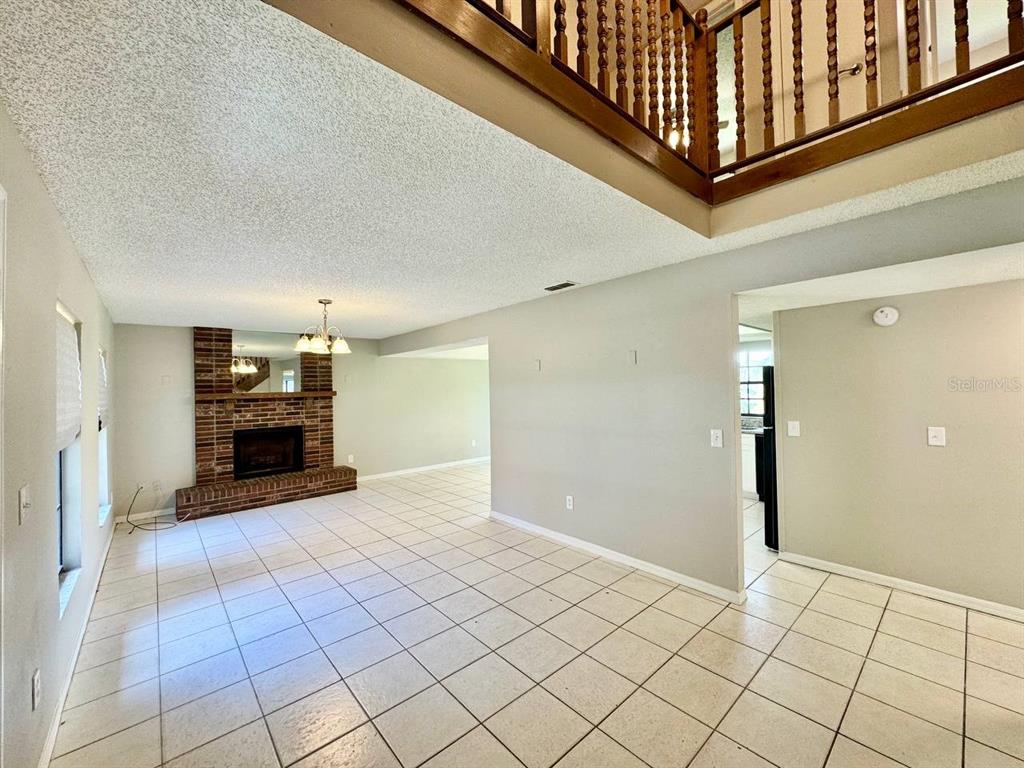 A living room with a brick fireplace, tiled floors, and a wooden staircase railing above — 5132 CHILKOOT STREET, TAMPA, FL
