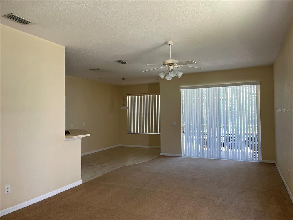 An open-concept living room with beige carpet, a ceiling fan, and sliding glass patio doors — 1628 N HAMPTON DRIVE, DAVENPORT, FL